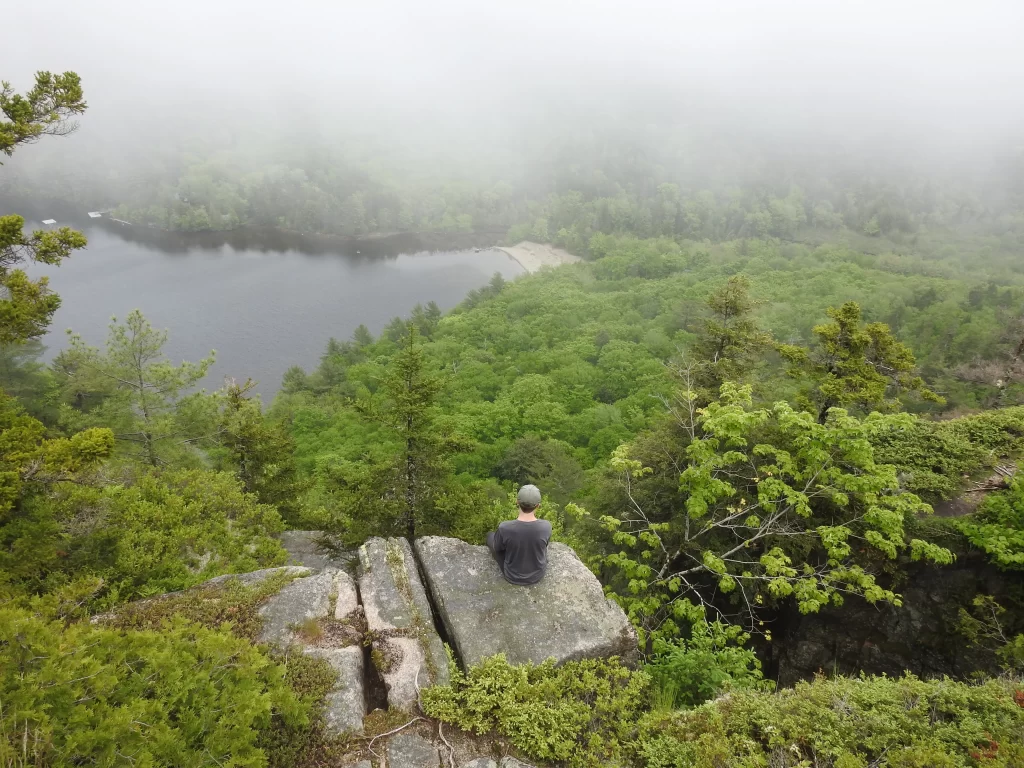 A photo of me perched on a rock overlooking a forested lake.